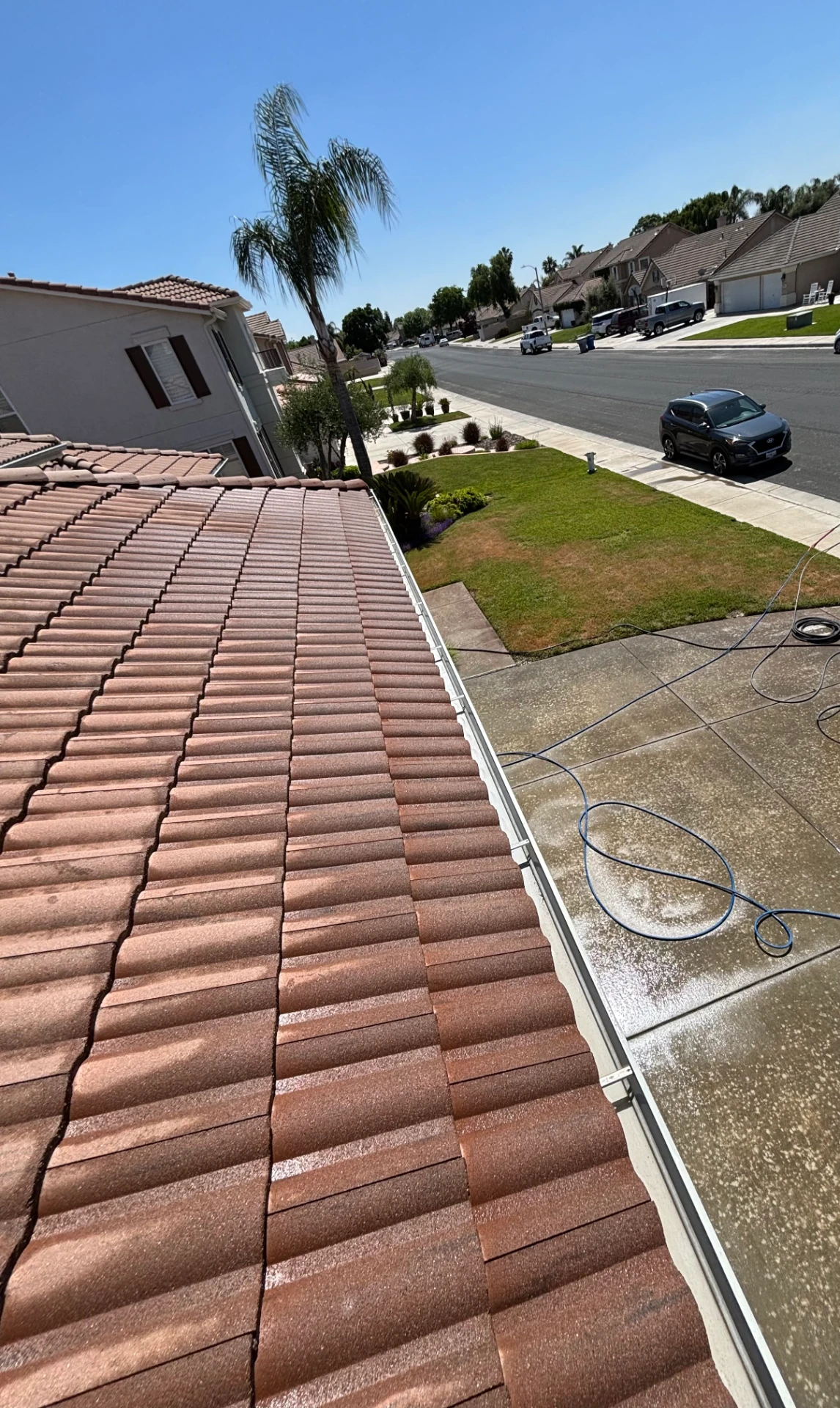 Freshly cleared rain gutter running along a tile roof edge above a rinsed driveway on a Central Valley home