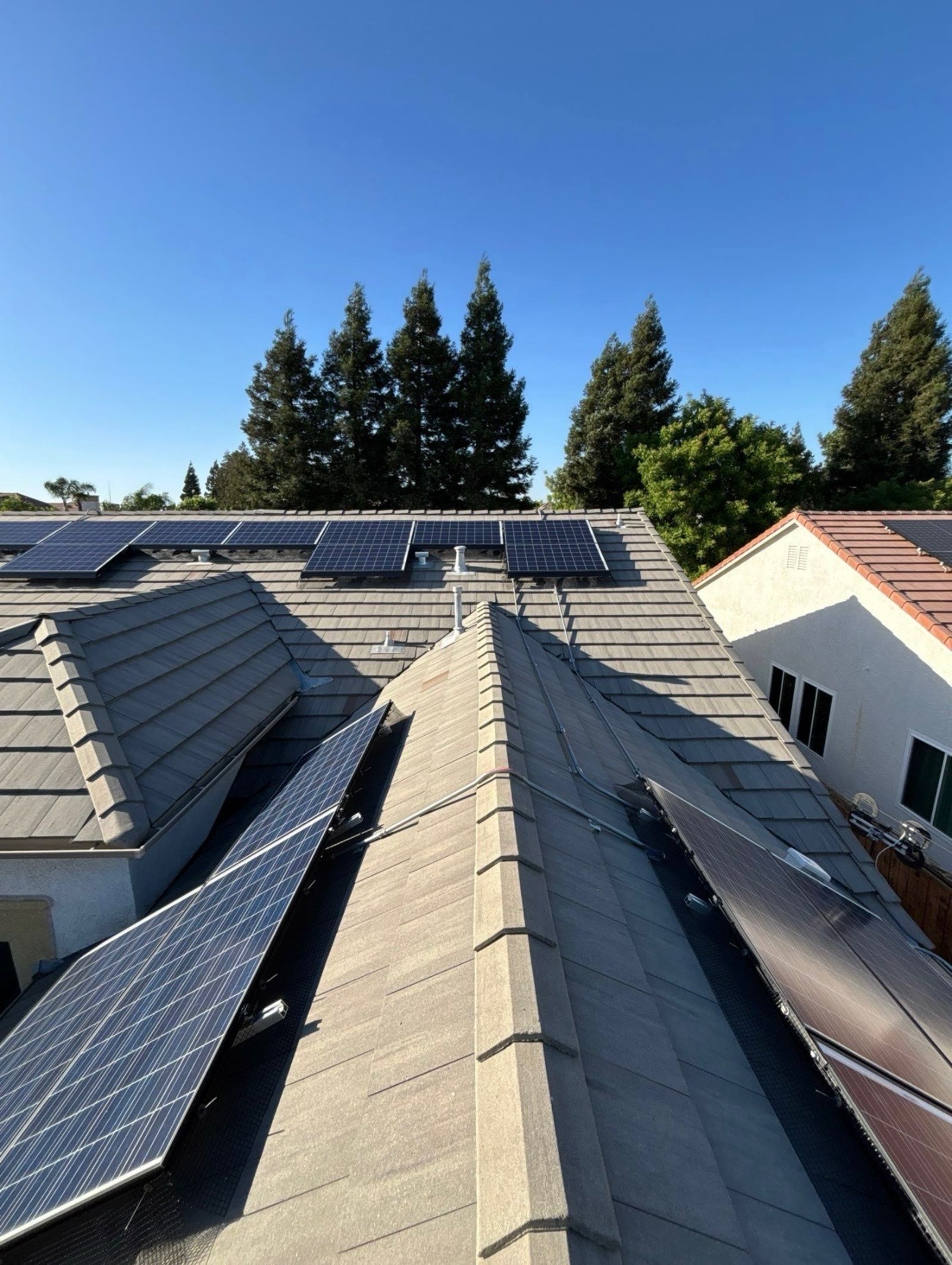 Solar panels across several roof slopes with clean, evenly dark glass under a blue sky