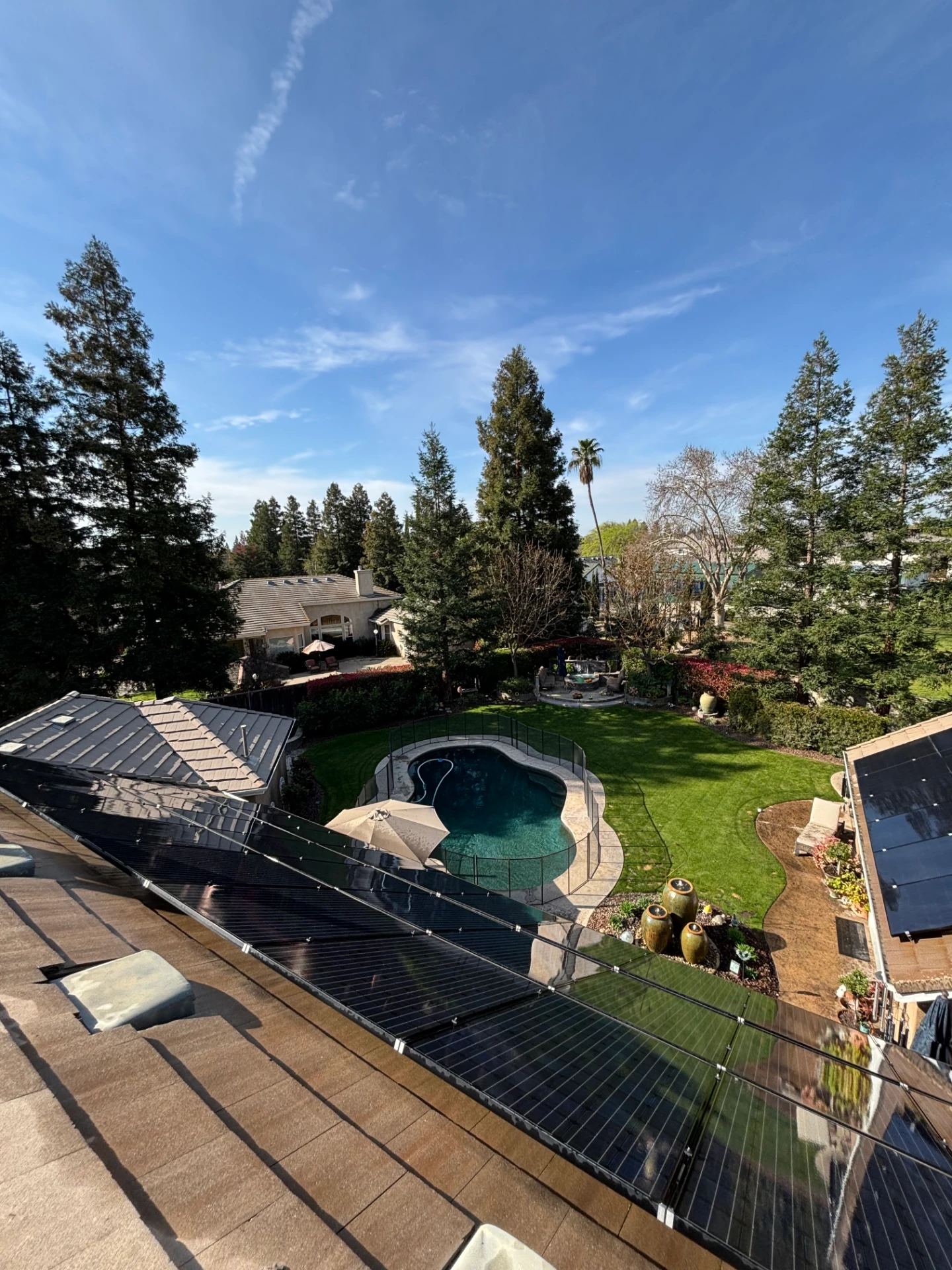 Rooftop view over a freshly maintained backyard with pool, lawn, and solar panels on a clear day